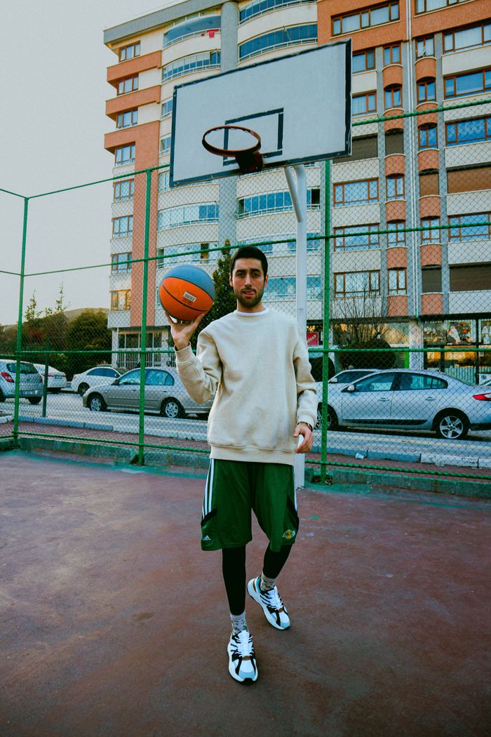 About Man holding a basketball in a city court, set against residential buildings.