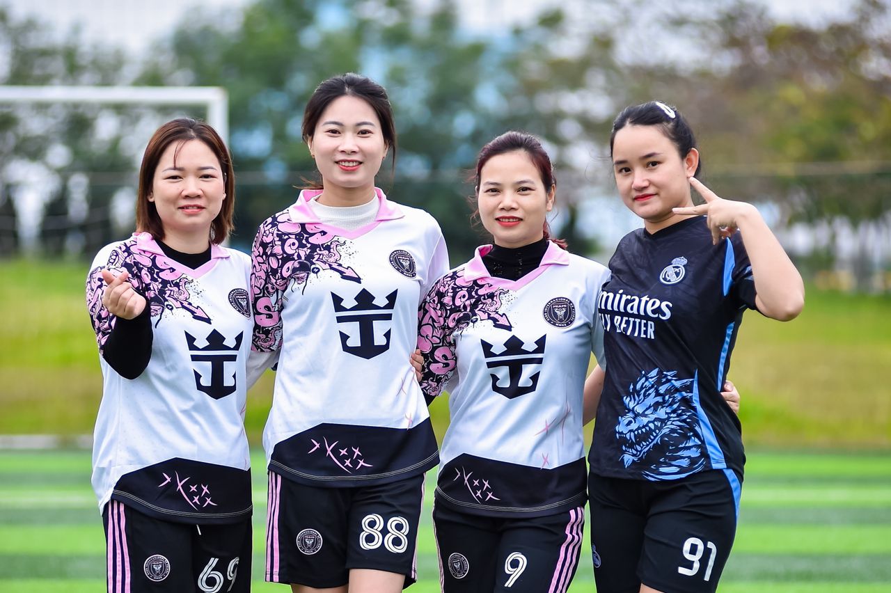 About Four women in football jerseys posing together on a soccer field in HÃ Ná»™i, Vietnam.